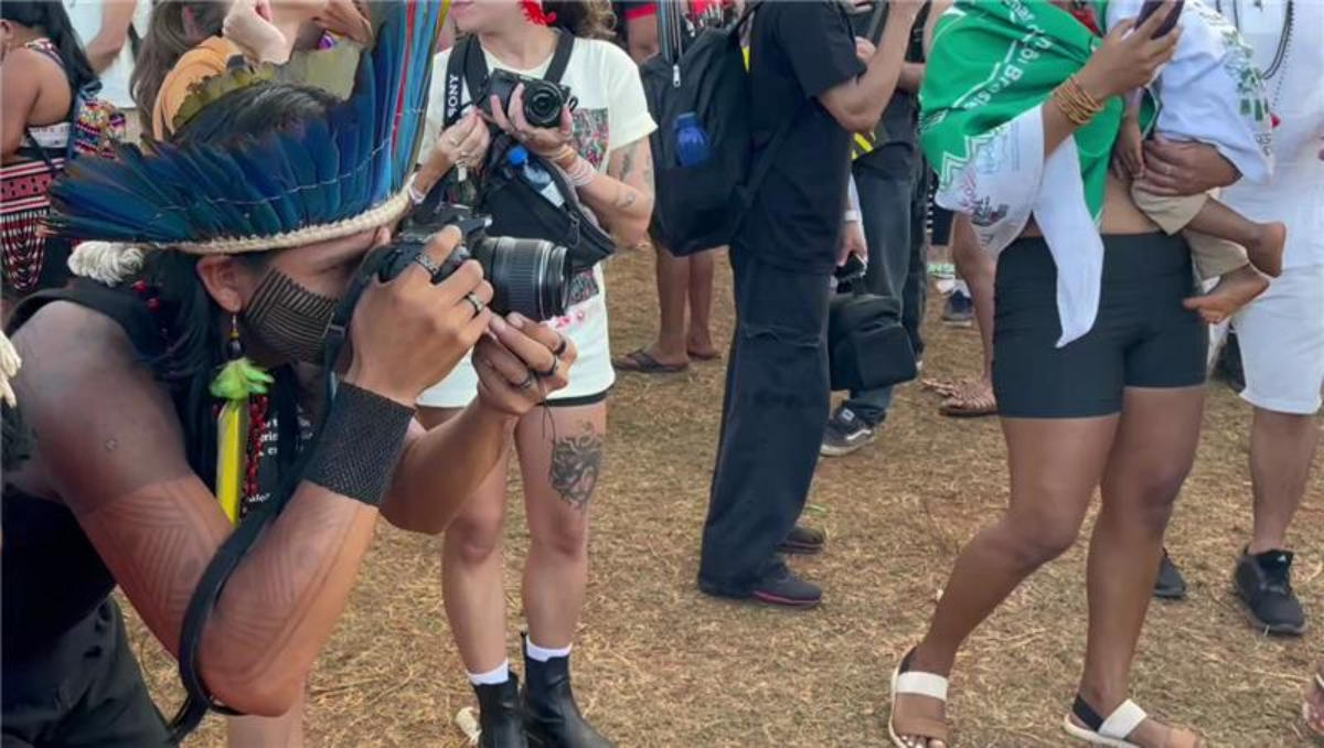 An Indigenous person takes photos from protestors at the Free Land Camp in Brasilia, Brazil, April 10, 2025. THOMSON REUTERS FOUNDATION/André Cabette Fábio
