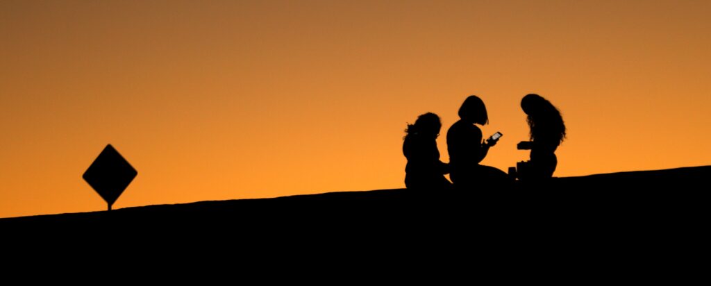 Young girls look at their phones as they sit on a hillside after sun set in El Paso, Texas, U.S., June 20, 2018.