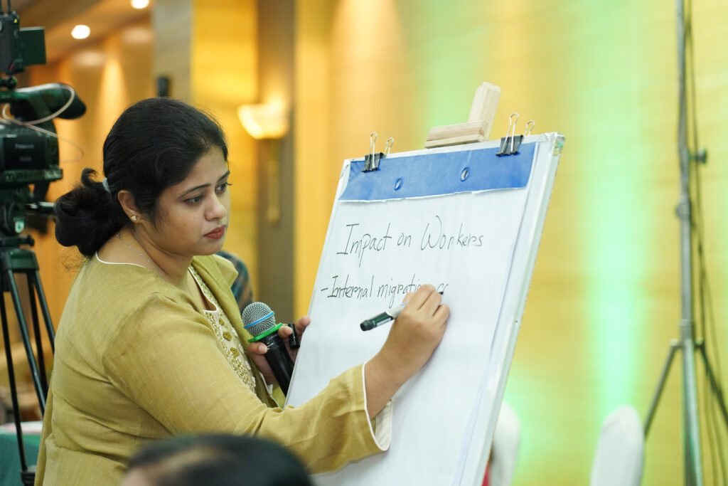 A woman in a yellow top writes the words 'impact on workers' and 'internation migration' on a flipchart