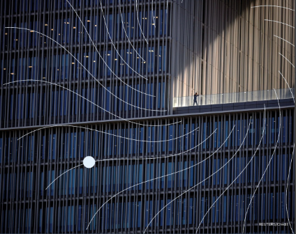 A man walks along the hallway of a high rise building with floor to ceiling windows.